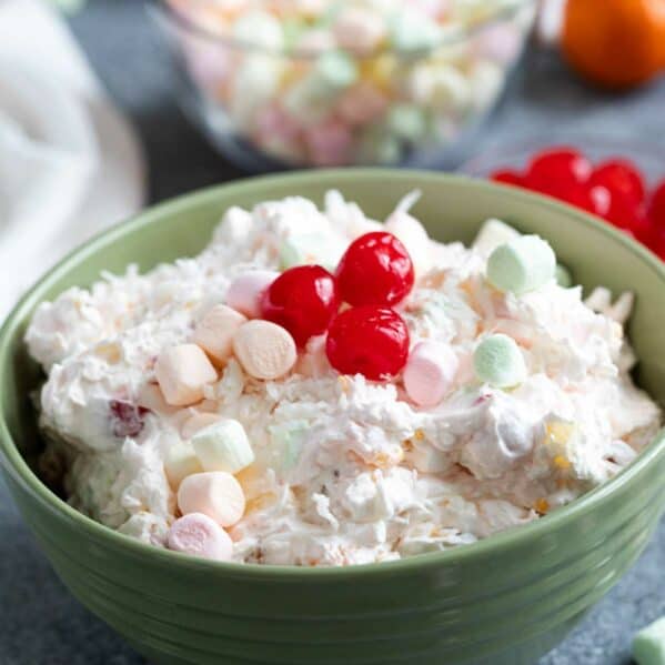 Green bowl filled with Ambrosia Salad, topped with maraschino cherries.