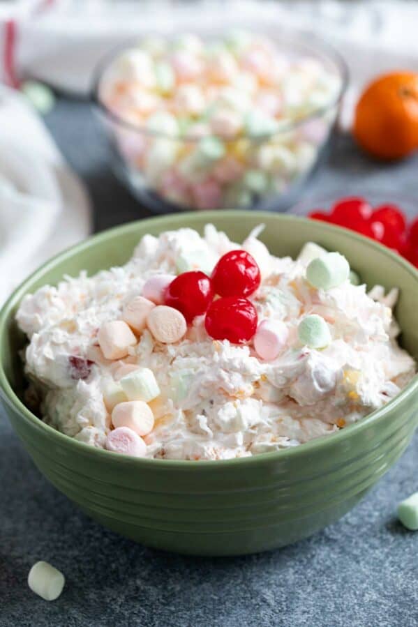 Green bowl filled with Ambrosia Salad, topped with maraschino cherries.