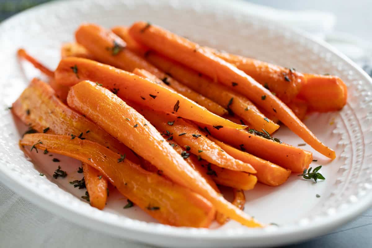 White serving dish with oven roasted carrots topped with thyme.