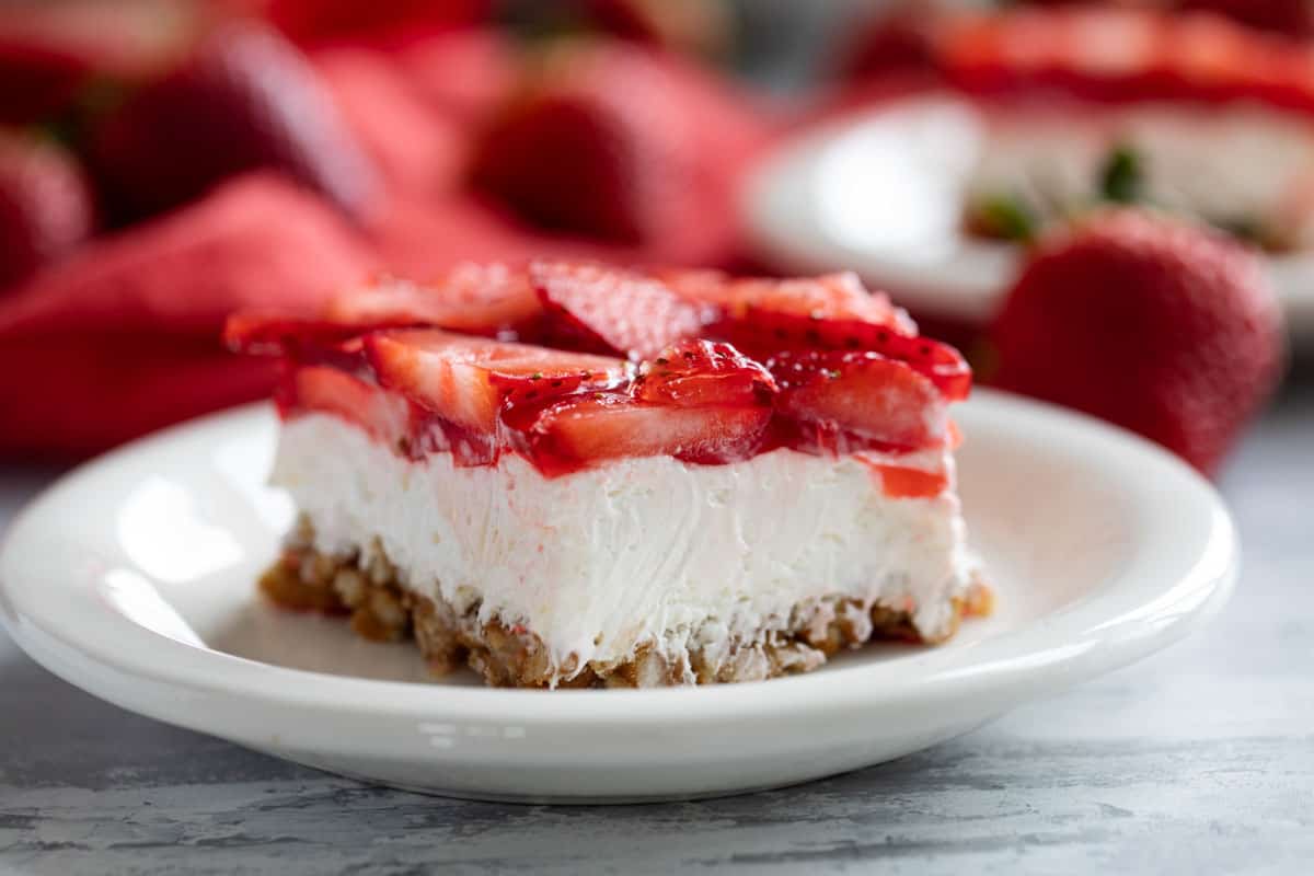 Slice of Strawberry Pretzel Salad with fresh strawberries in the background.
