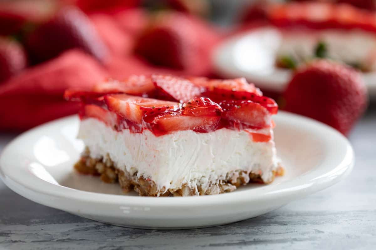 Sweet and salty, this Strawberry Pretzel Salad is as pretty as it is delicious. Serve it as a side dish or a dessert - either way, it’s always a hit! Slice of Strawberry Pretzel Salad with fresh strawberries in the background.