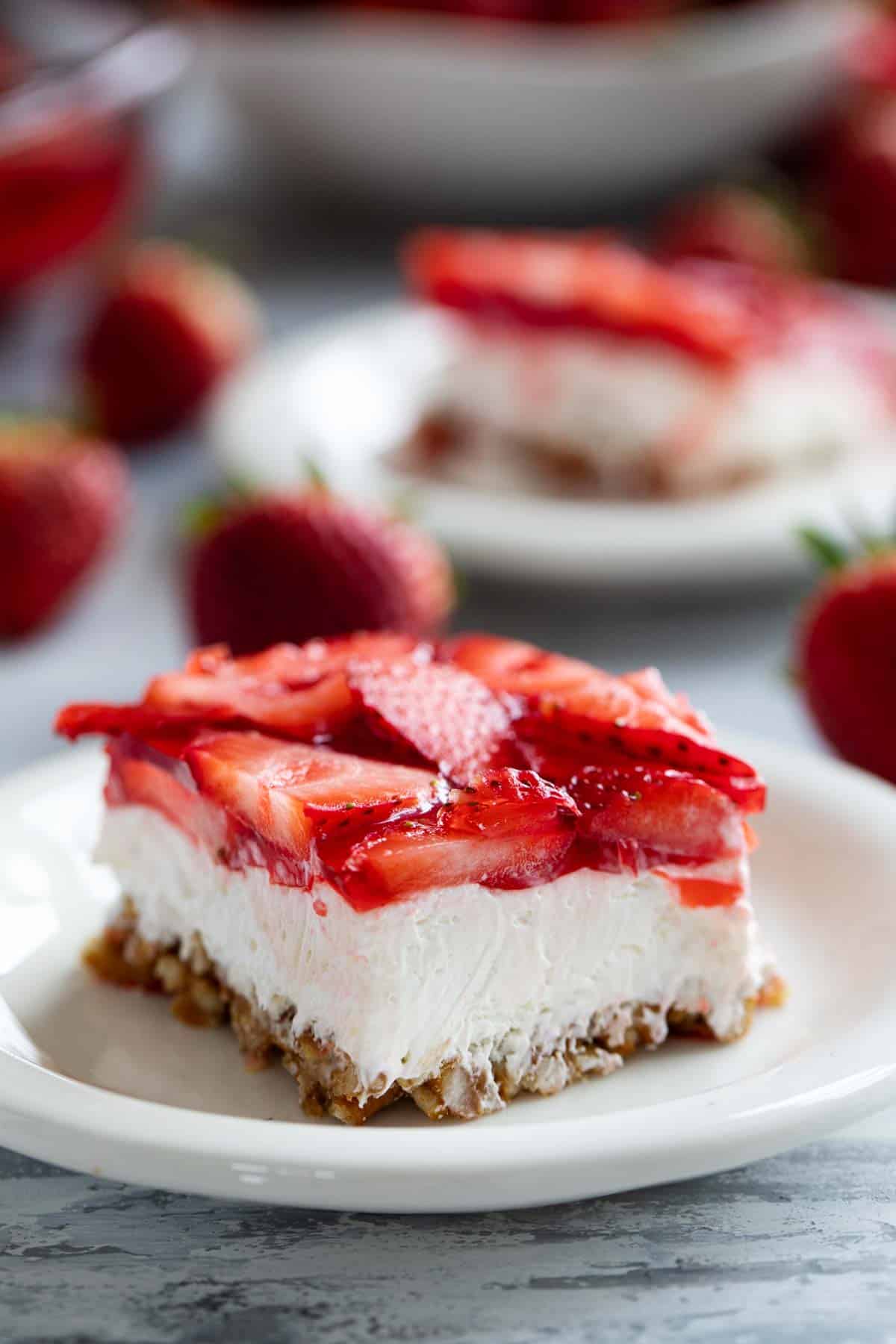 Slice of Strawberry Pretzel Salad on a plate with another slice in the background.