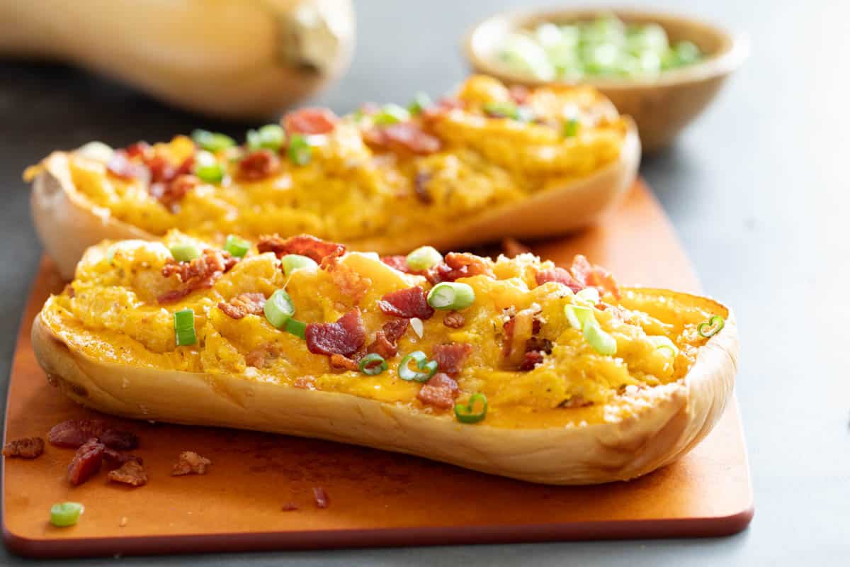 Roasted butternut squash is mashed with lots of cheese and bacon and then stuffed back into the squash skins and baked in this filling and comforting Stuffed Butternut Squash. Stuffed Butternut Squash halves on a cutting board.