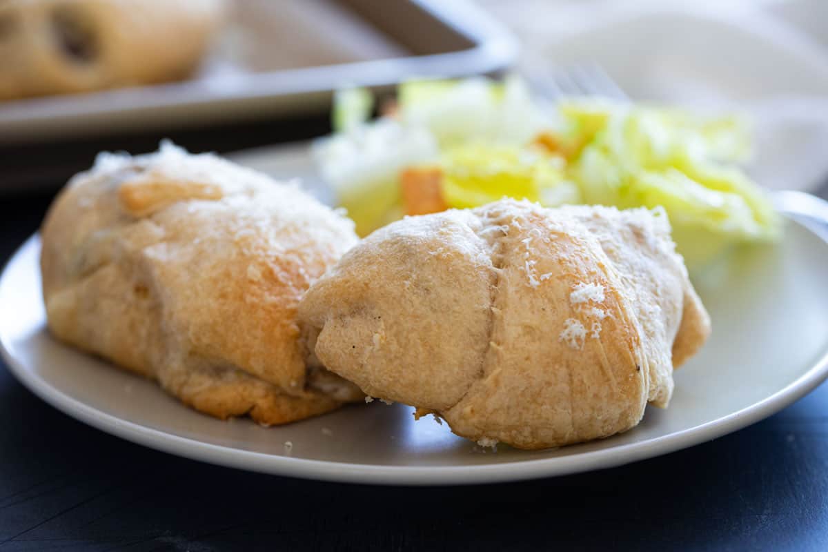 Two chicken crescent rolls on a plate with salad.