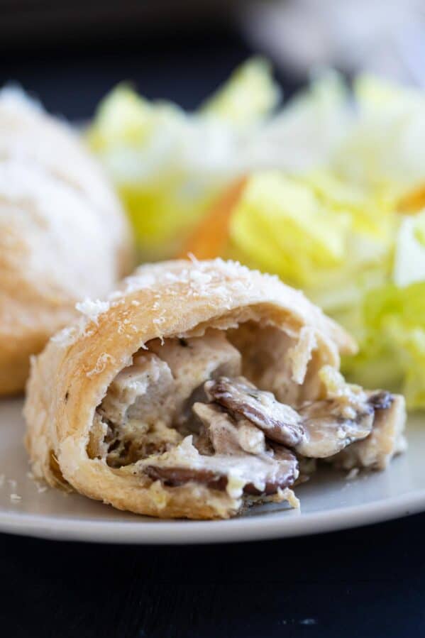 Chicken crescent roll on a plate with a bite taken from it showing the inside.