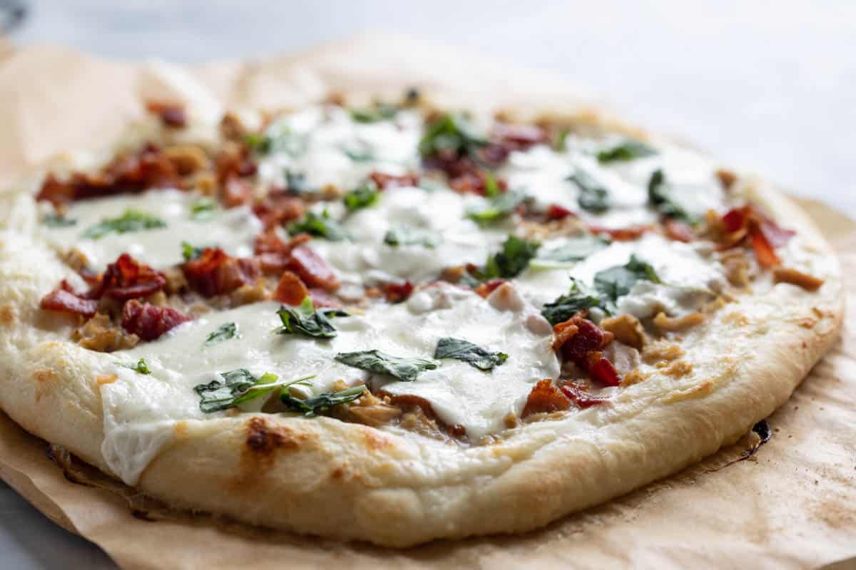 This Clam Pizza with Bacon is an unexpected pizza combination. Clams are combined with smoky bacon and a creamy alfredo sauce for a pizza recipe that is perfect for seafood lovers. Clam Pizza with Bacon topped with mozzarella and basil.