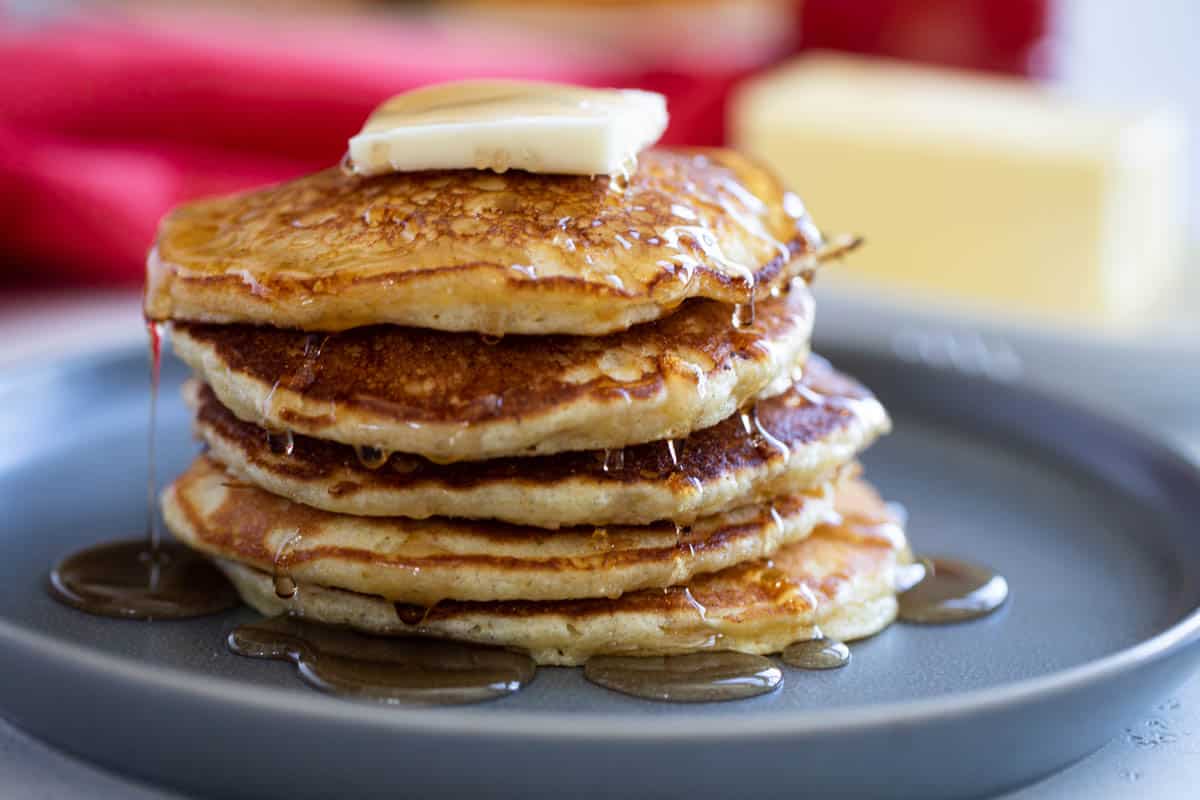 Stack of cornmeal pancakes with a pat of butter on top and maple syrup over the top.