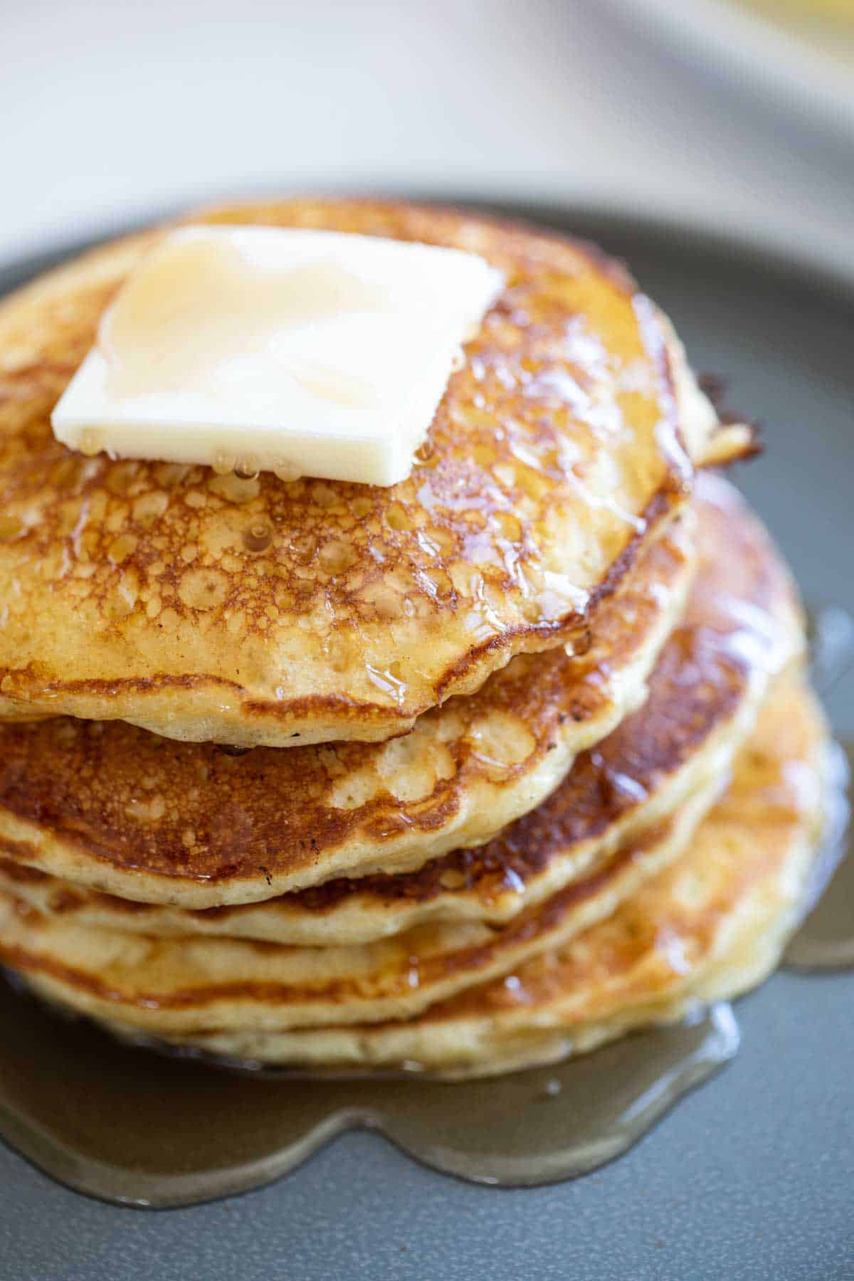 Stack of cornmeal pancakes topped with butter and syrup.