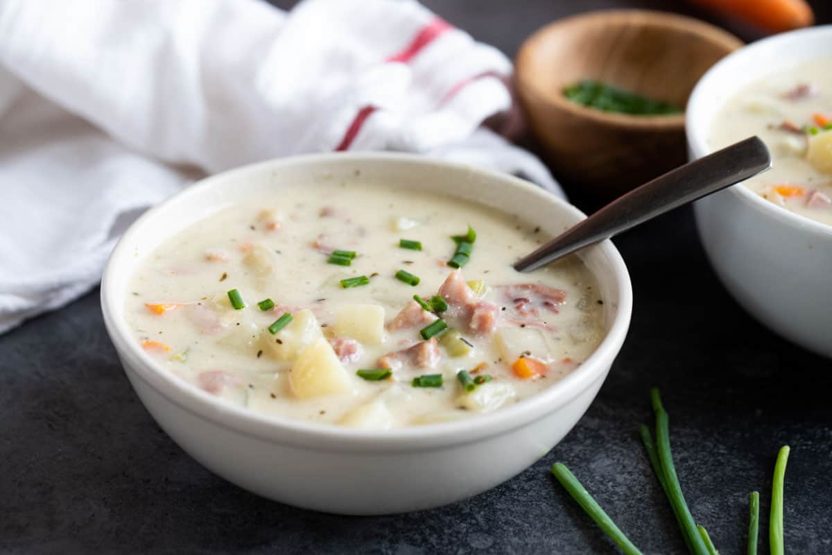 White bowl with ham and potato soup topped with chives.