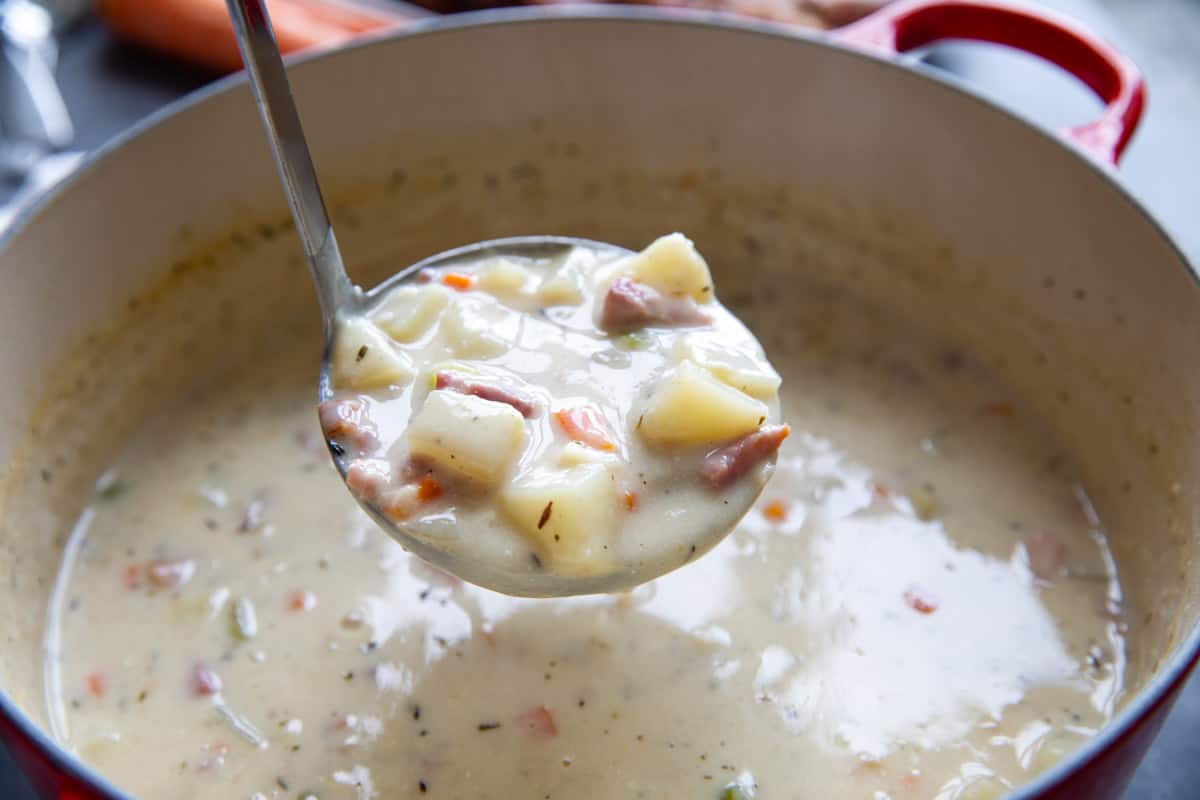 Pot filled with ham and potato soup with a ladle full of soup.