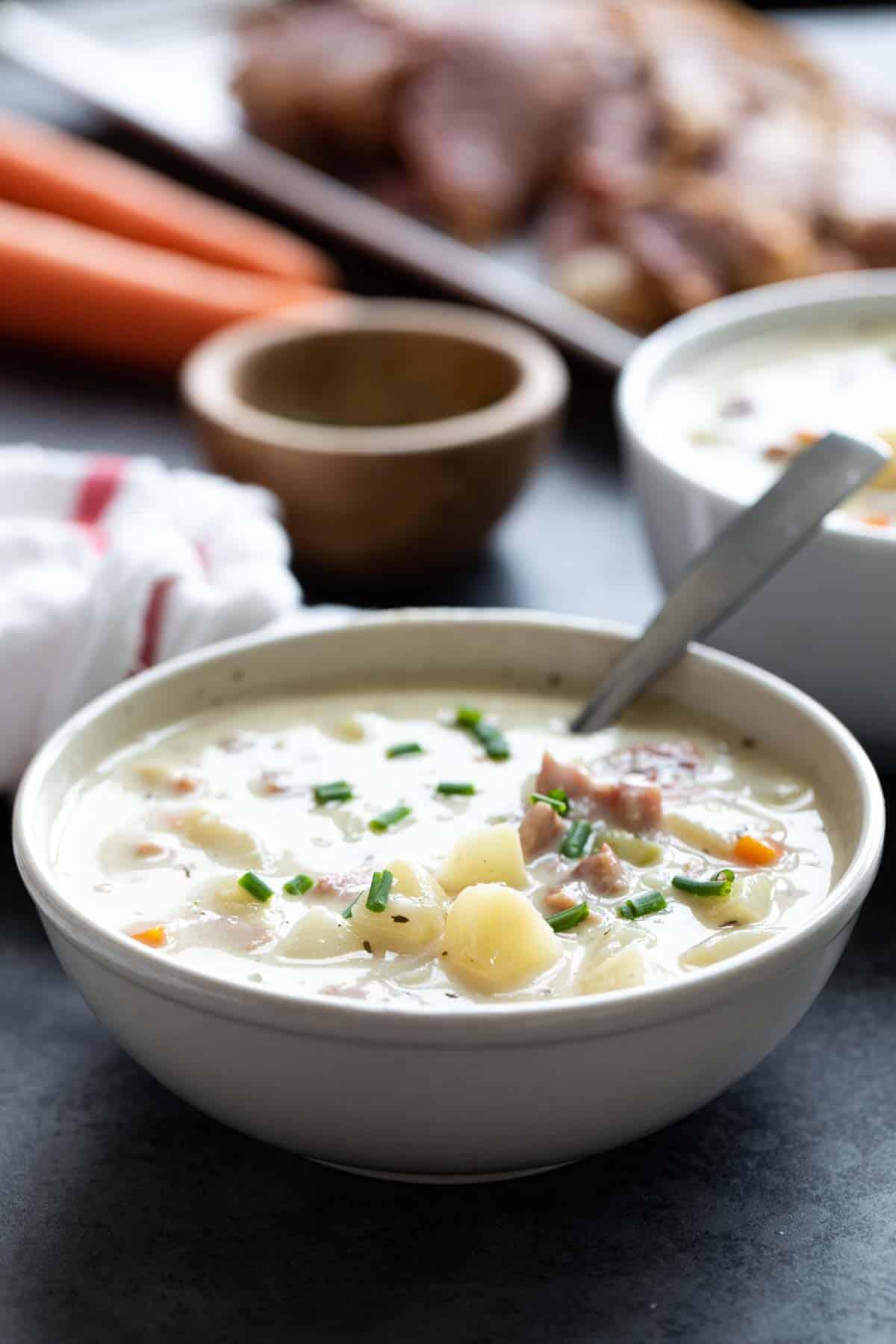 Bowl of ham and potato soup with a spoon in it.