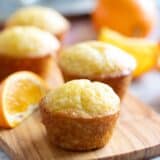 Orange muffins with an orange simple syrup on a wooden board.