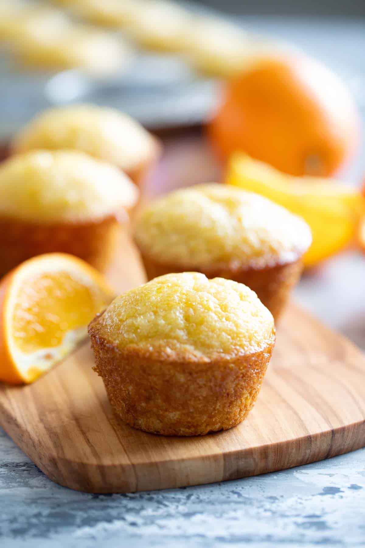 Orange muffins with an orange simple syrup on a wooden board.