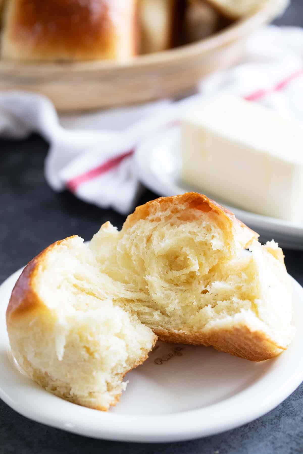 Potato roll on a small plate, torn in half to show texture.