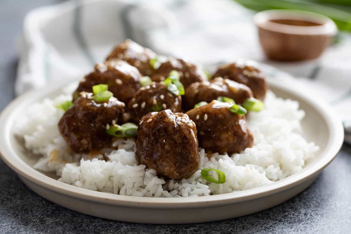 Plate with Teriyaki Meatballs on top of rice, then topped with green onions and toasted sesame seeds.