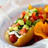 Bacon, lettuce, avocado, and tomato topped hot dog in a parchment paper lined basket.