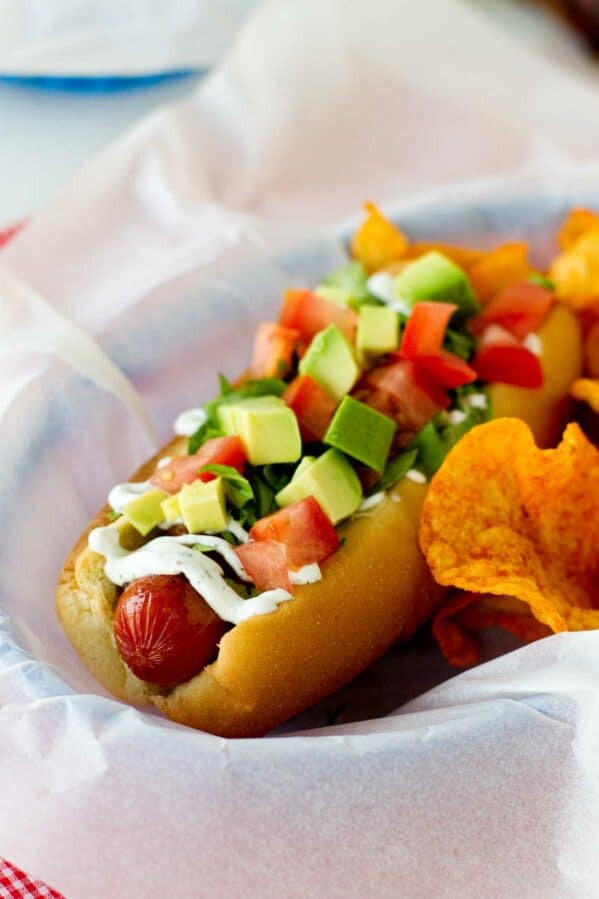 Bacon, lettuce, avocado, and tomato topped hot dog in a parchment paper lined basket.