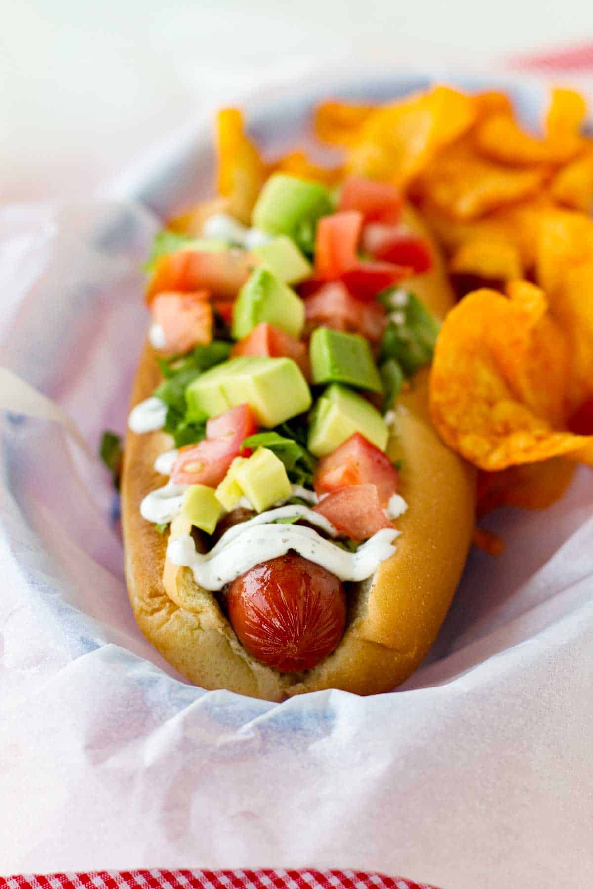 Hot dog topped with bacon, lettuce, avocado, and tomato.