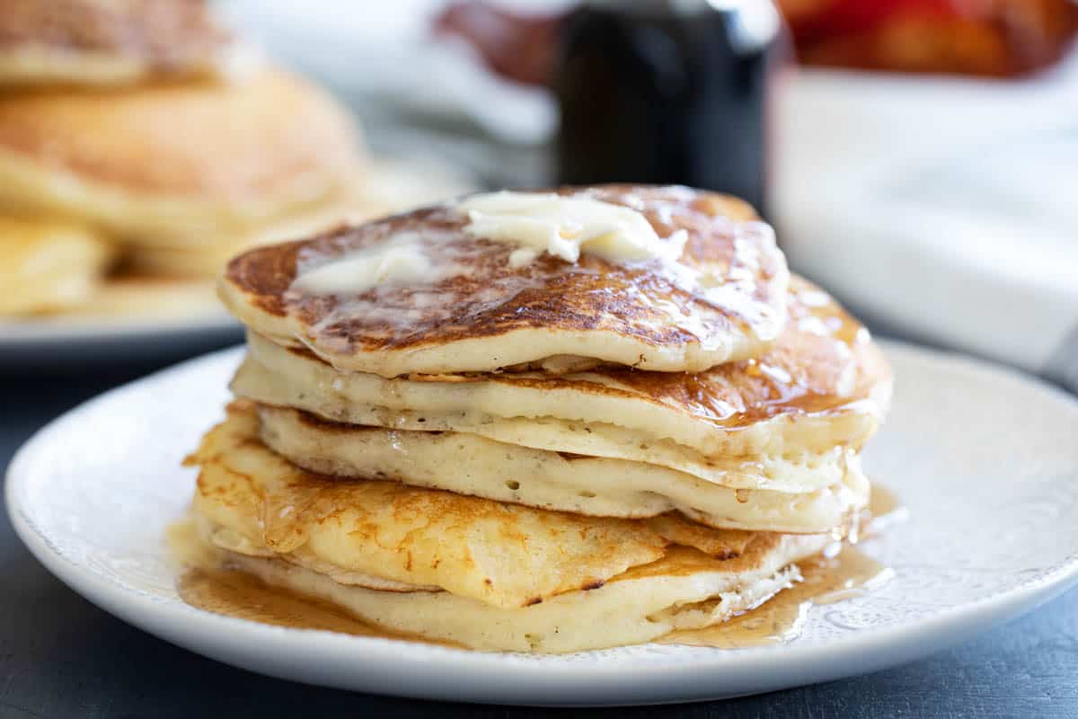 Stack of 5 fluffy homemade buttermilk pancakes topped with syrup and butter.