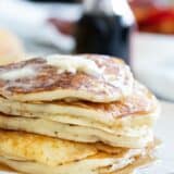 Stack of buttermilk pancakes topped with butter and syrup on a plate.