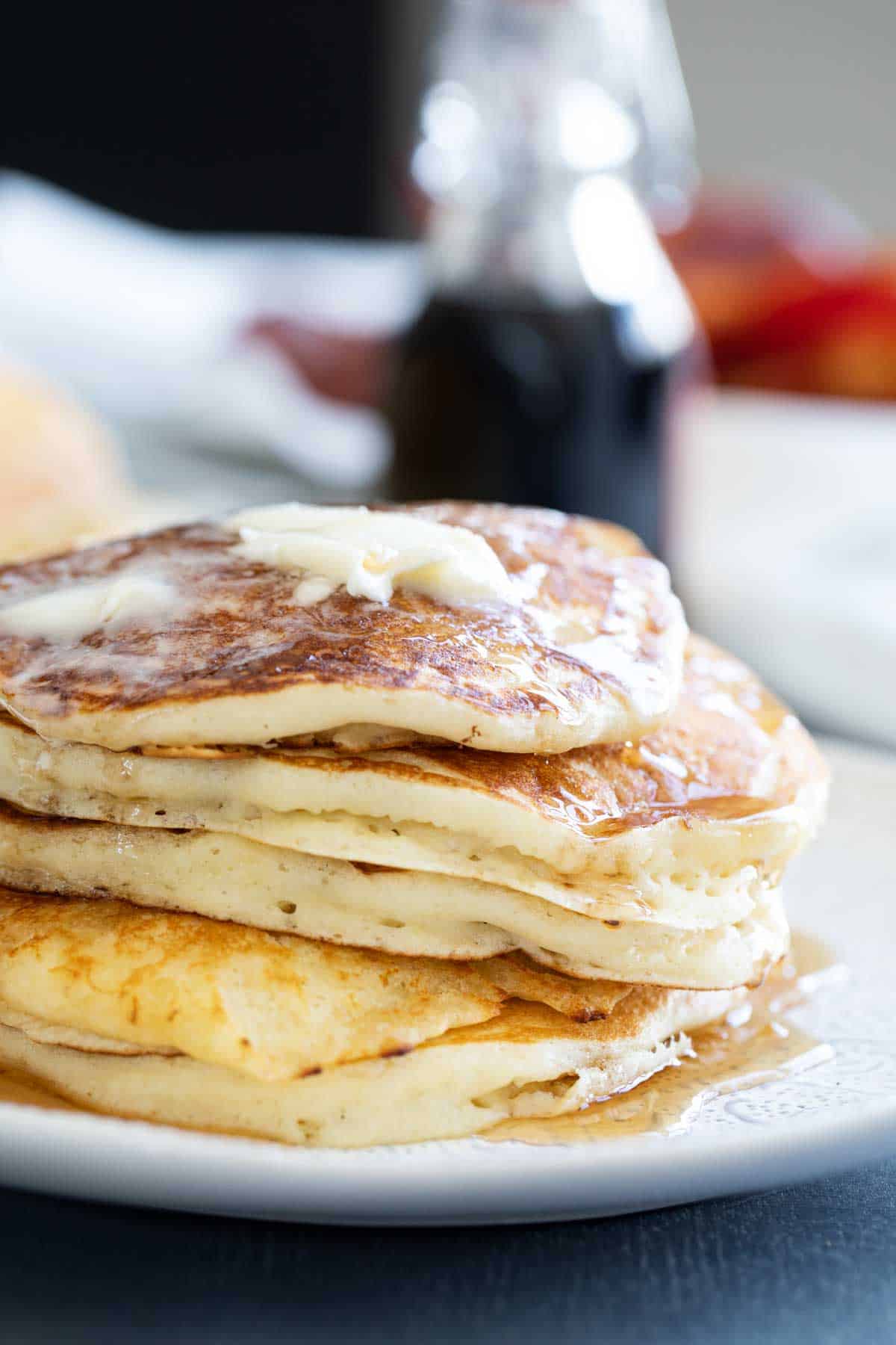 Stack of buttermilk pancakes topped with butter and syrup on a plate.