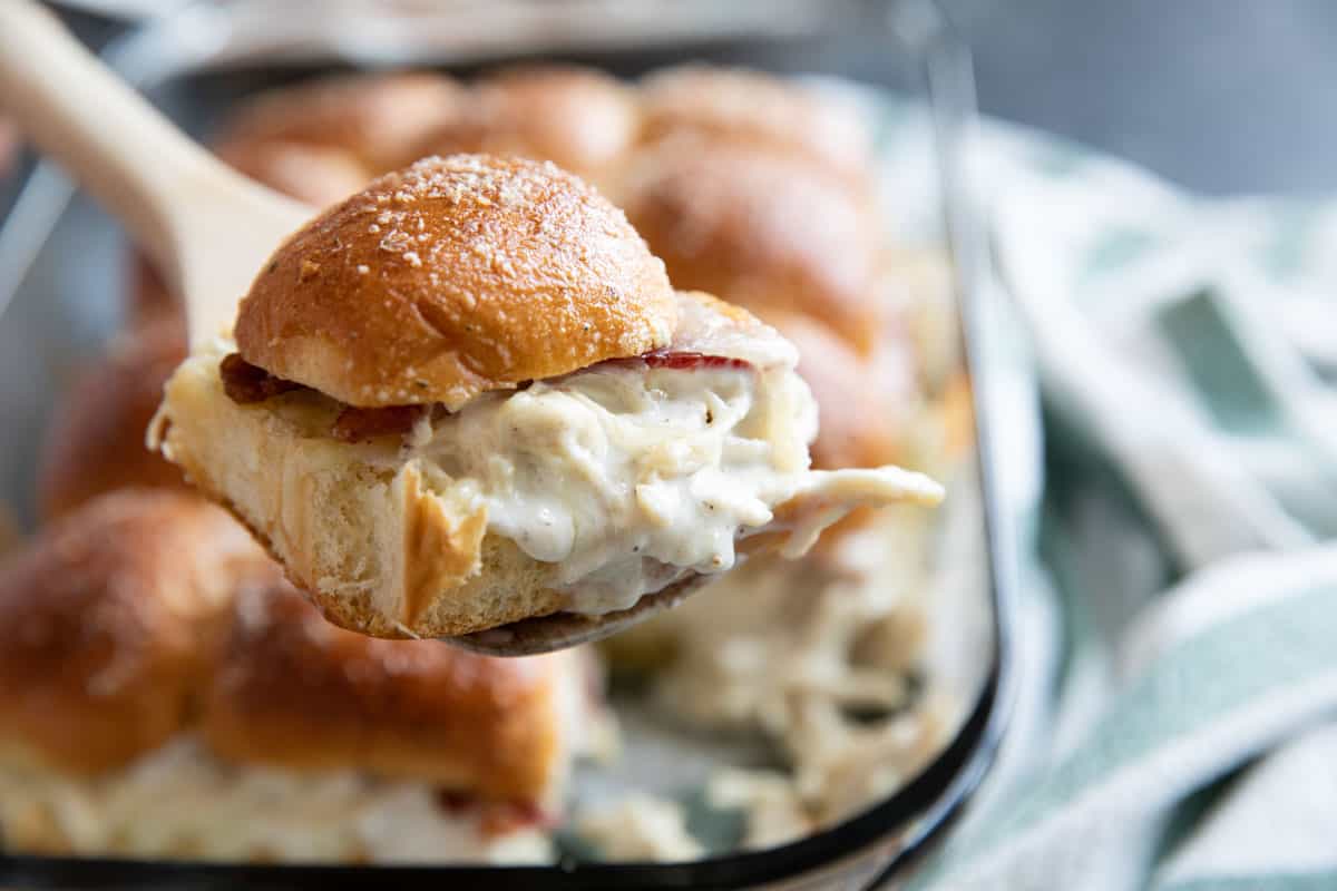 Chicken bacon ranch slider being taken from a baking dish on a wooden spatula.