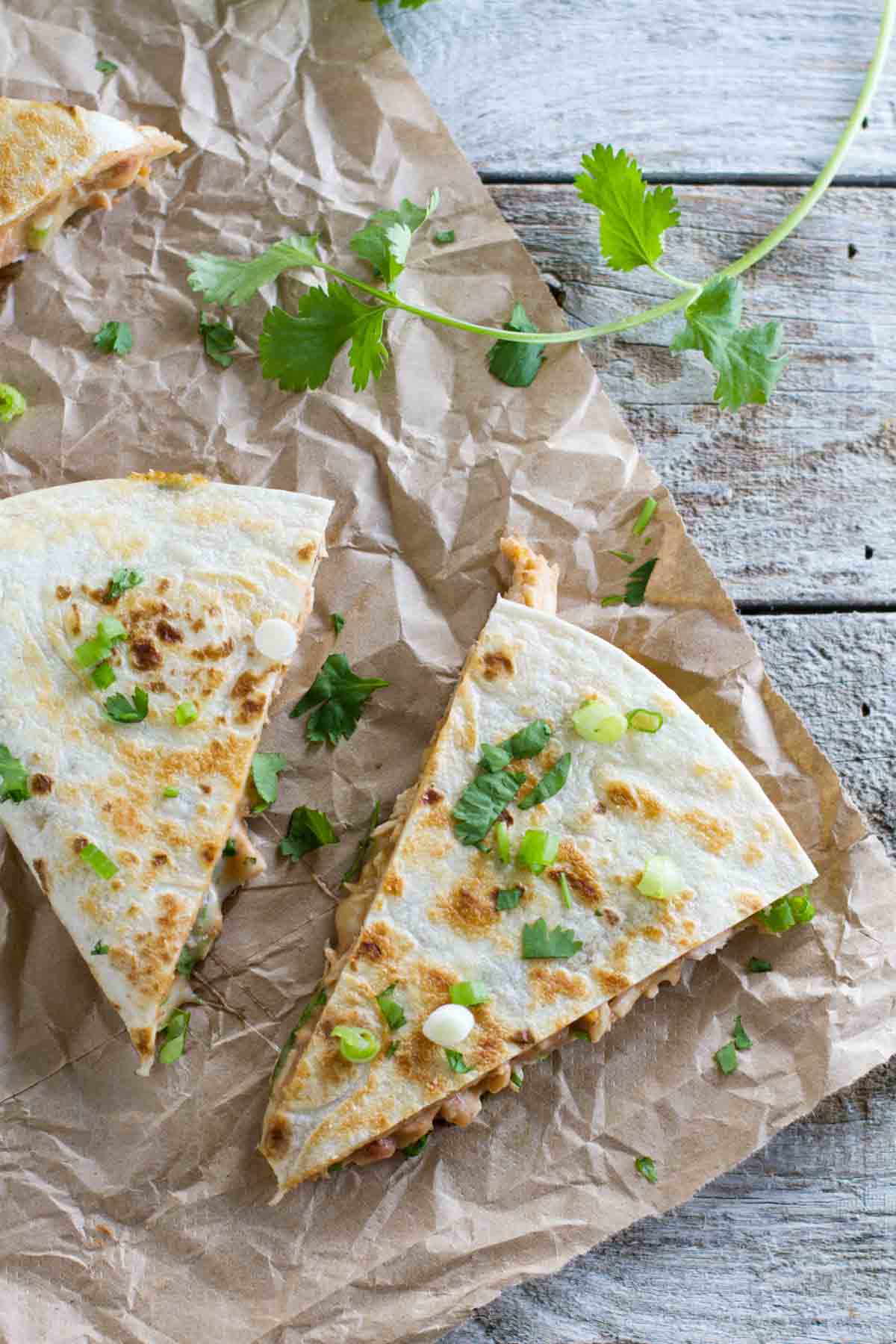 Chicken quesadilla with refried beans cut into wedges with cilantro and green onion on top.