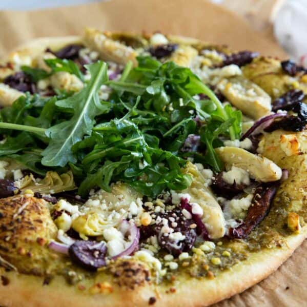 Mediterranean Pizza on parchment paper topped with arugula.