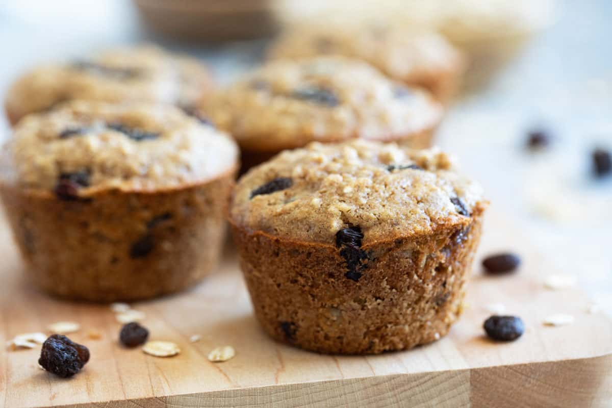 Oatmeal raisin muffins on a wooden board with raisins on the side.