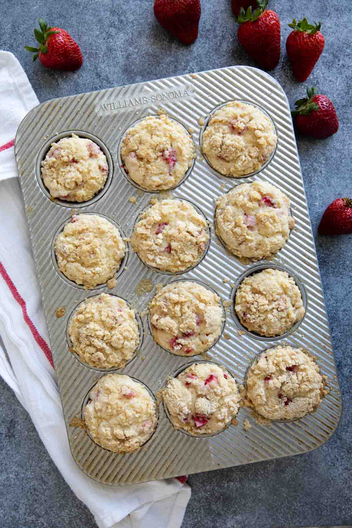 Strawberry muffins in a muffin tin with a white towel.