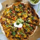 Full taco pizza topped with sour cream, guacamole, lettuce, and pico de gallo.