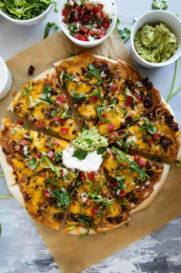 Full taco pizza topped with sour cream, guacamole, lettuce, and pico de gallo.