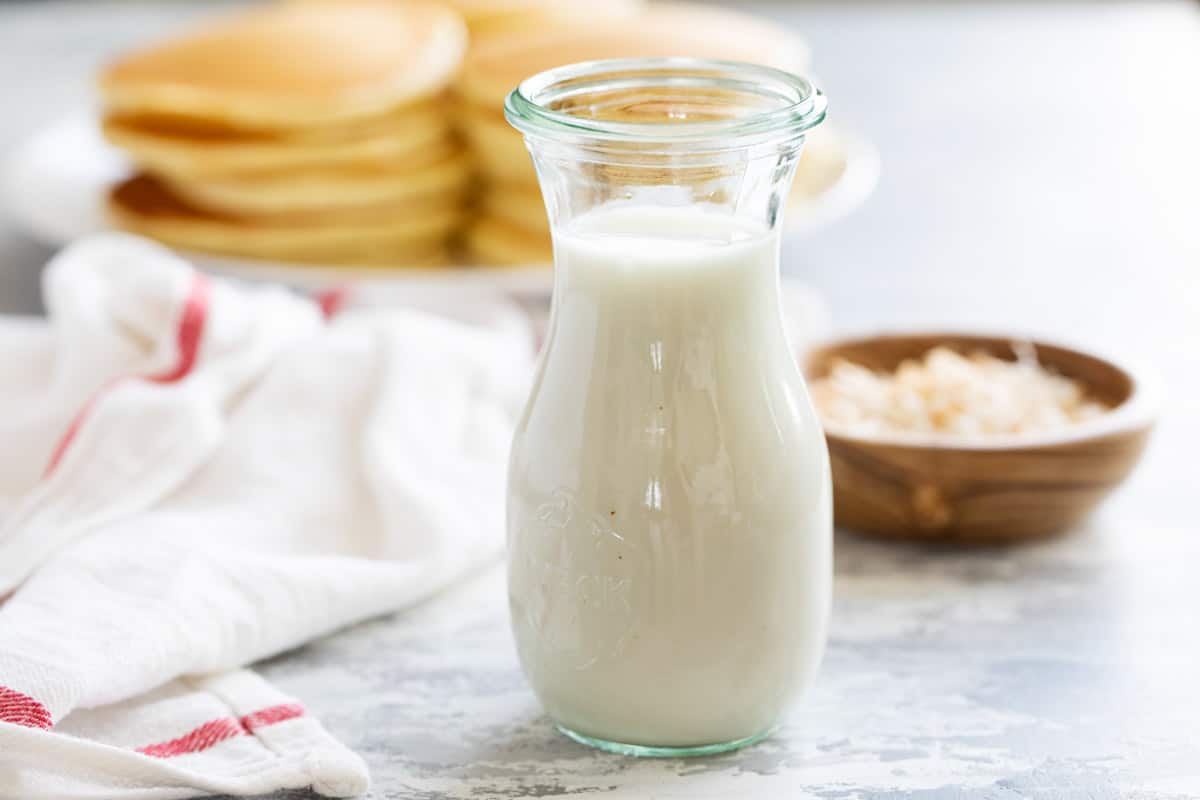 Container full of coconut syrup with pancakes in the background.