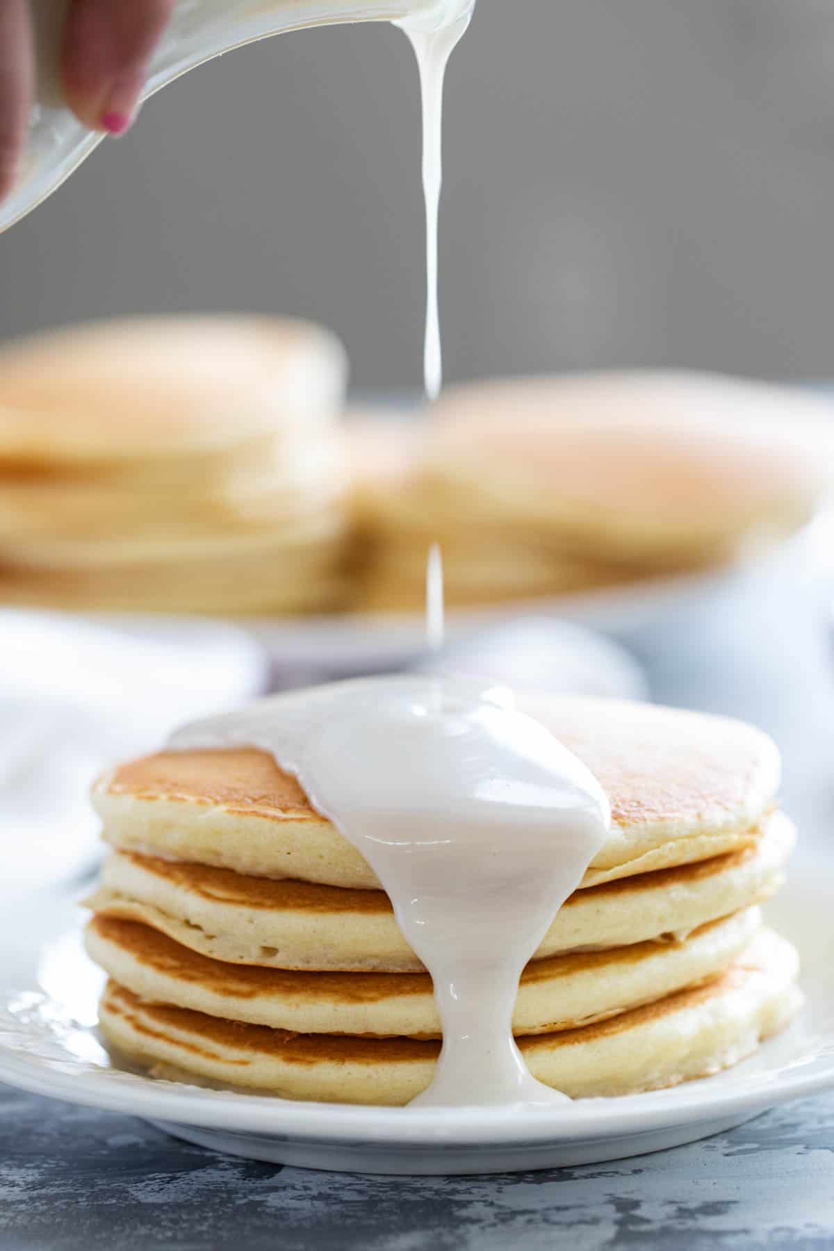 Pouring coconut syrup on a stack of pancakes.