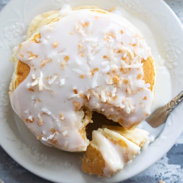 Stack of pancakes topped with coconut syrup and toasted coconut with a fork full of pancakes.