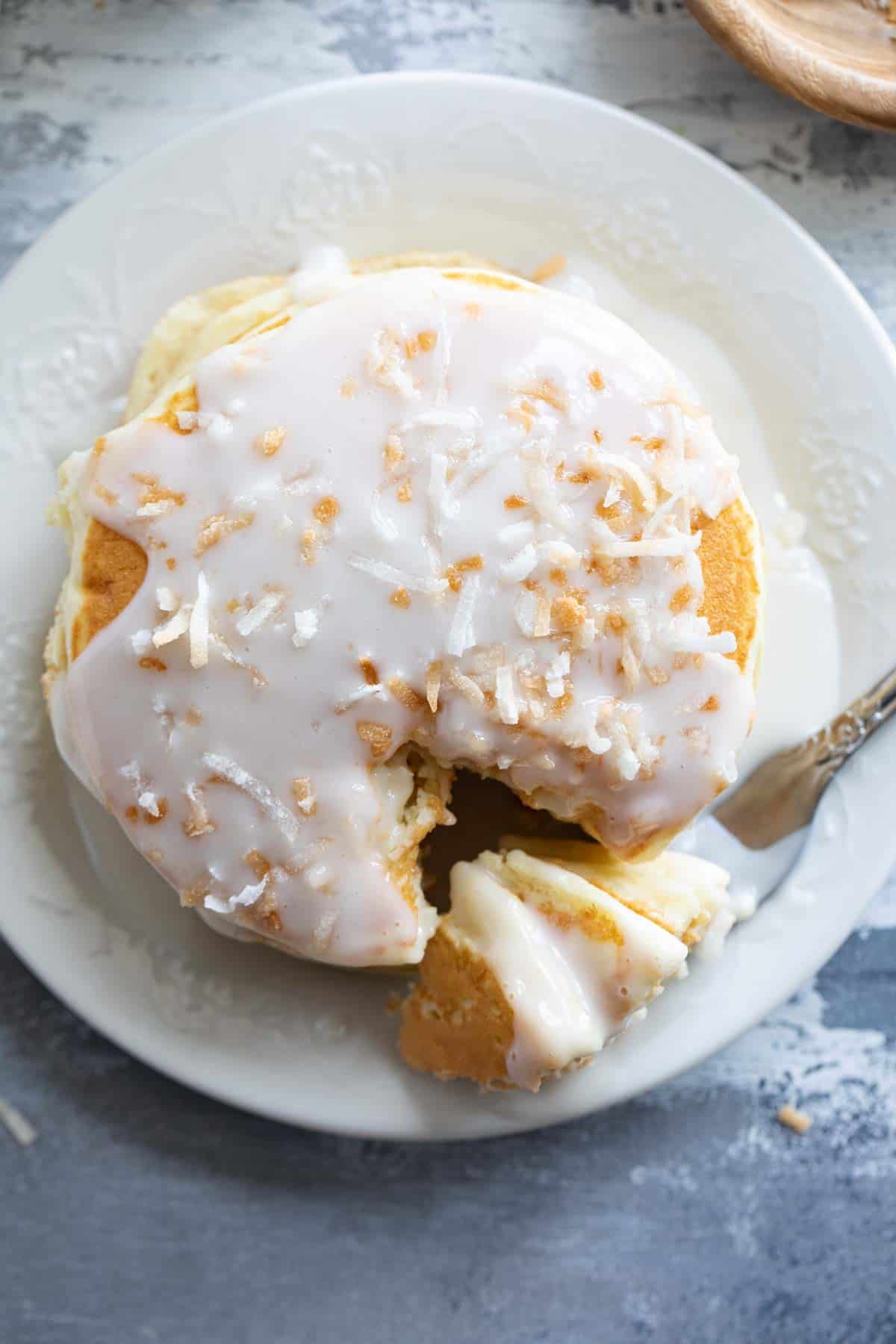 Stack of pancakes topped with coconut syrup and toasted coconut with a fork full of pancakes.