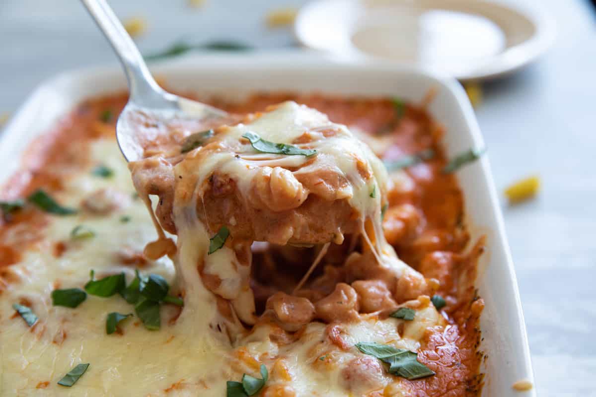 Baking dish with pizza pasta and serving spoon scooping the pasta out.