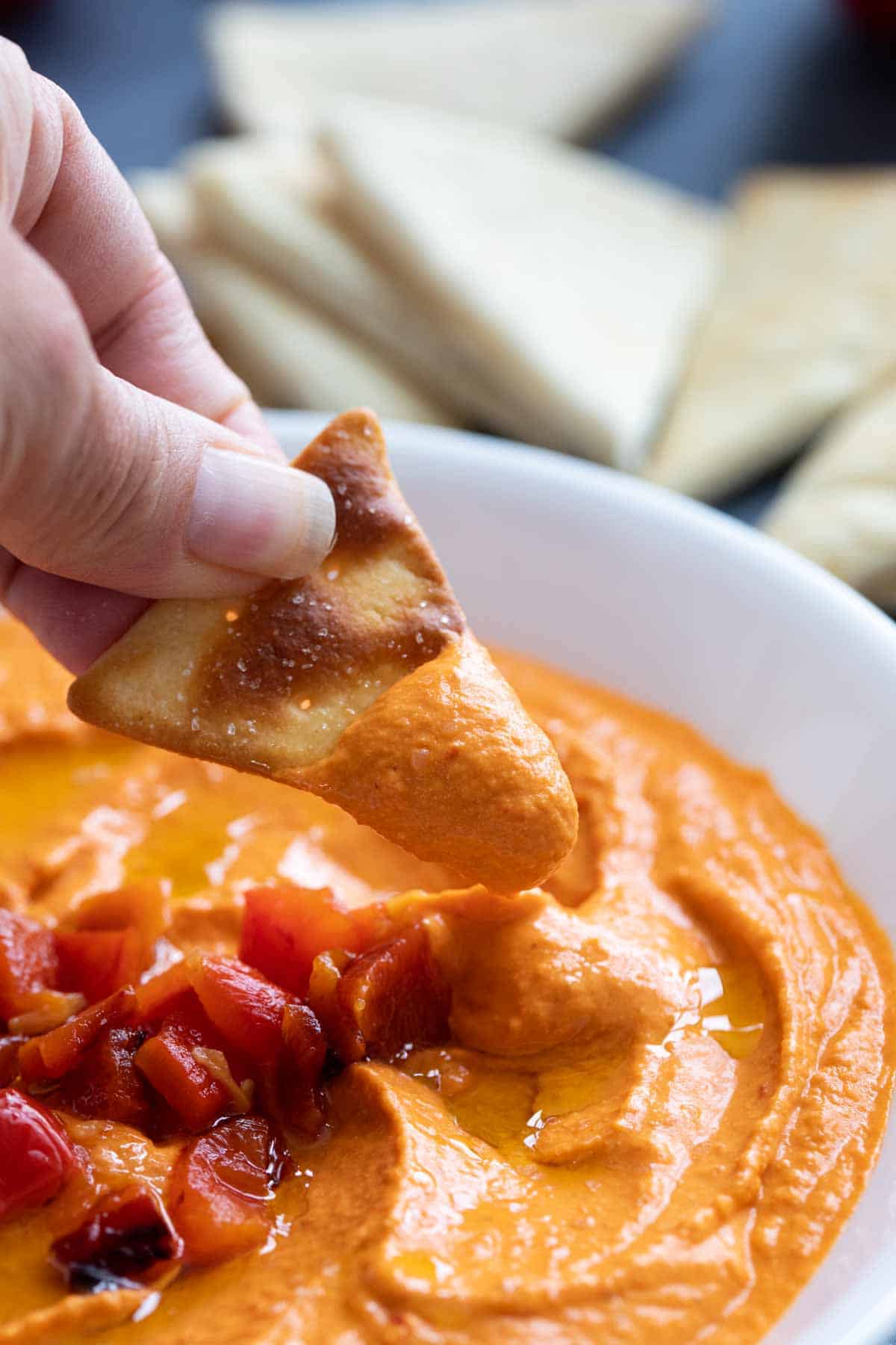 Dipping a pita chip into roasted red pepper hummus.