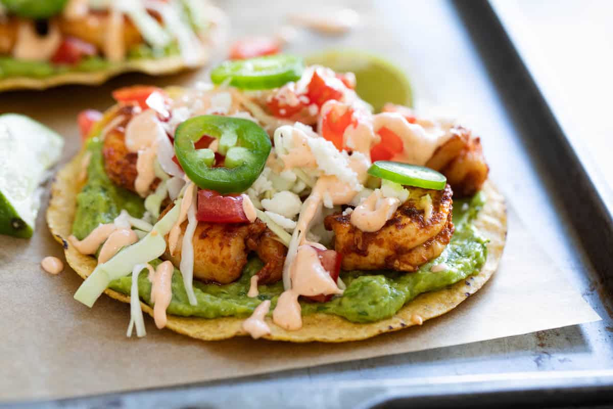 Shrimp Tostada topped with jalapenos and a homemade sauce on parchment paper.