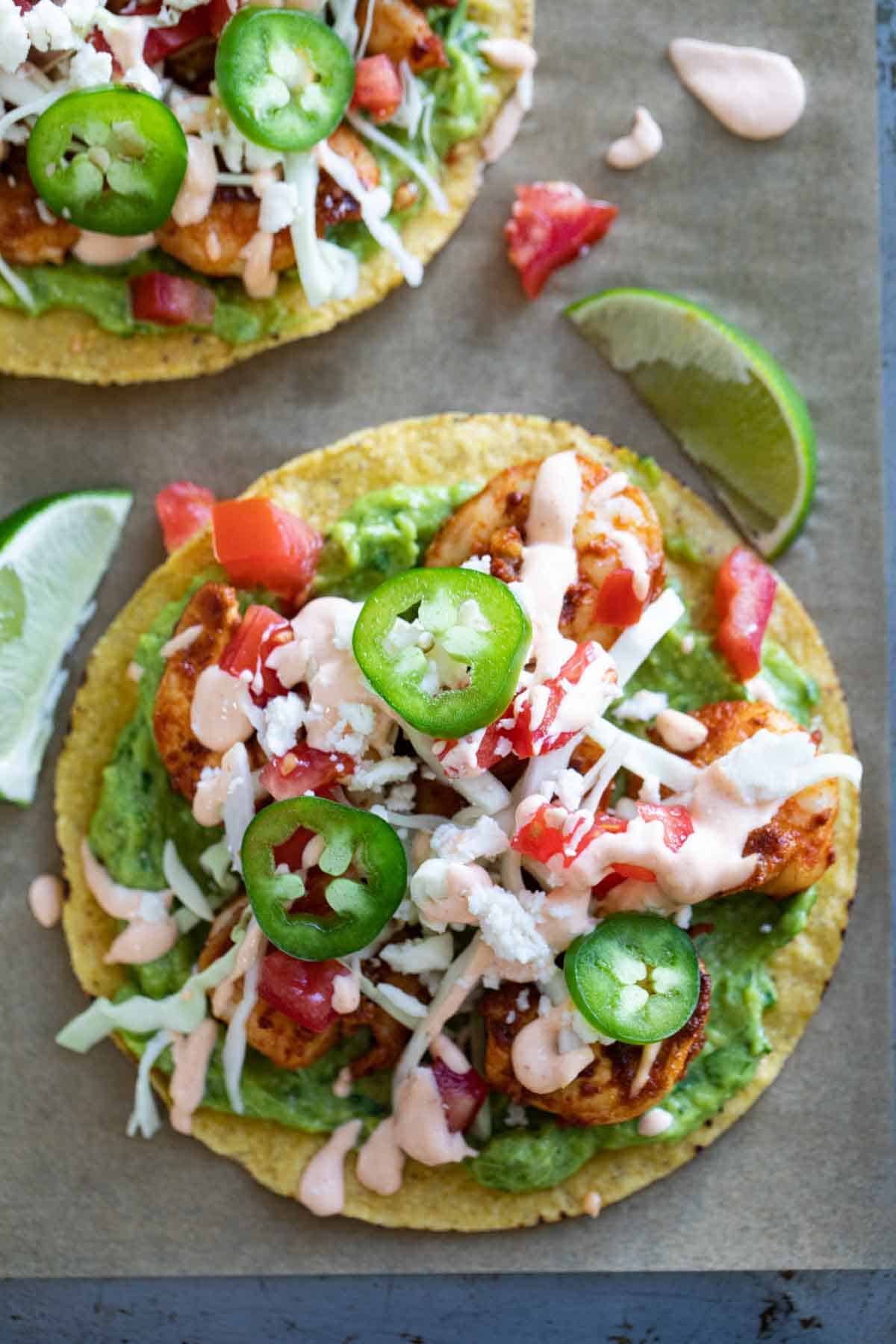 Two shrimp tostadas topped with cabbage, tomatoes, jalapenos, cheese, and sauce.