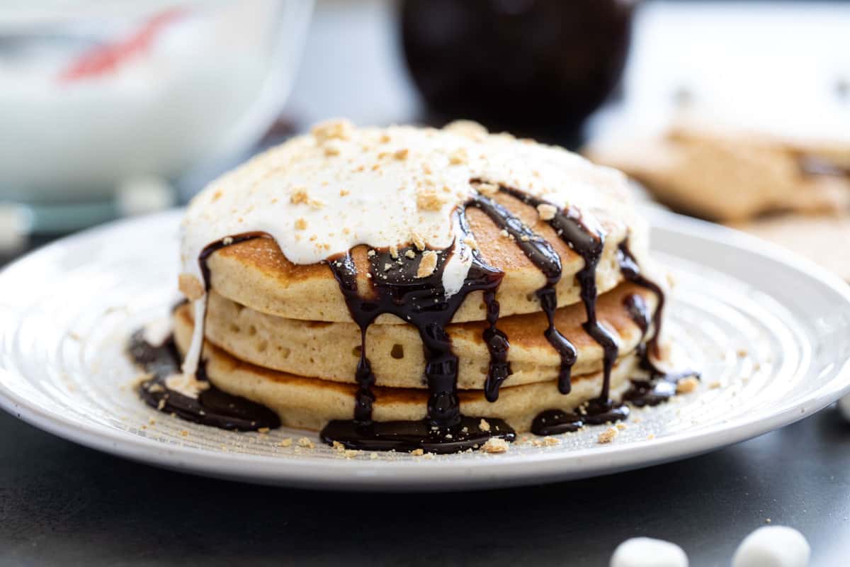 S'mores pancakes - three graham cracker pancakes topped with chocolate sauce, marshmallow sauce, and crushed graham crackers.