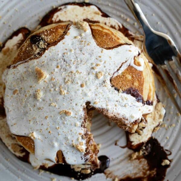 S'mores pancakes topped with chocolate sauce and marshmallow sauce.