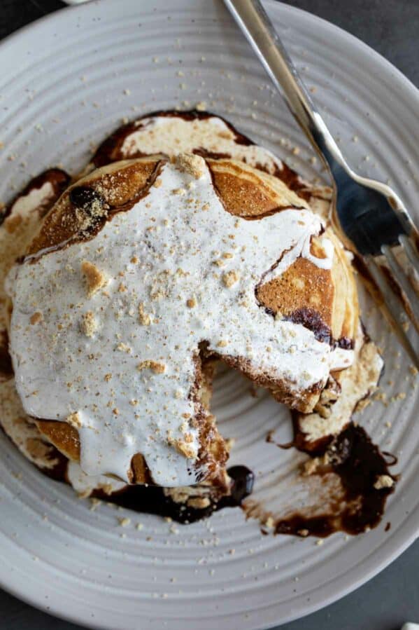 S'mores pancakes topped with chocolate sauce and marshmallow sauce.