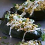 A line of stuffed poblano peppers on a baking sheet. the peppers are filled with chicken and cheese and topped with lime cream.