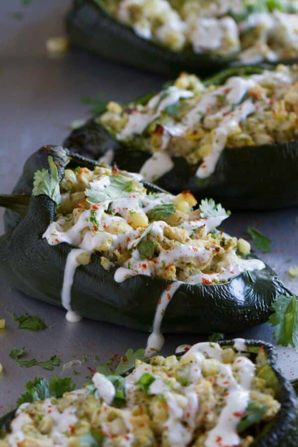 A line of stuffed poblano peppers on a baking sheet. the peppers are filled with chicken and cheese and topped with lime cream.