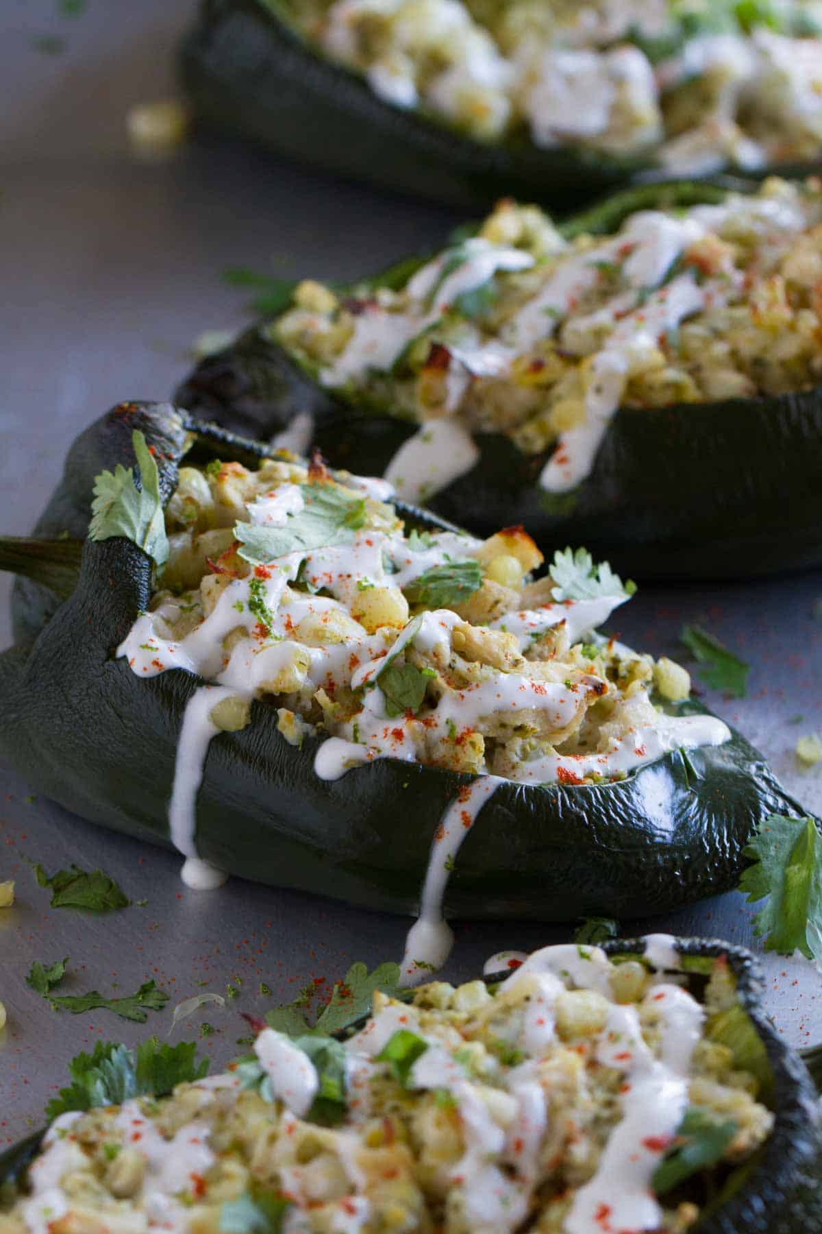 Flavor explosion! These Stuffed Poblano Peppers with Chicken and Corn are packed with flavor – chicken, corn, cheese and salsa all inside a mild poblano pepper. Don’t skip the lime cream! A line of stuffed poblano peppers on a baking sheet. the peppers are filled with chicken and cheese and topped with lime cream.