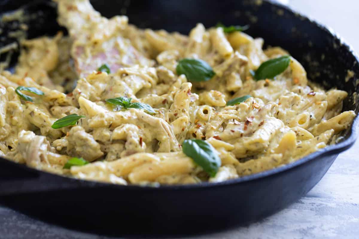 Skillet filled with chicken pesto pasta topped with fresh basil.