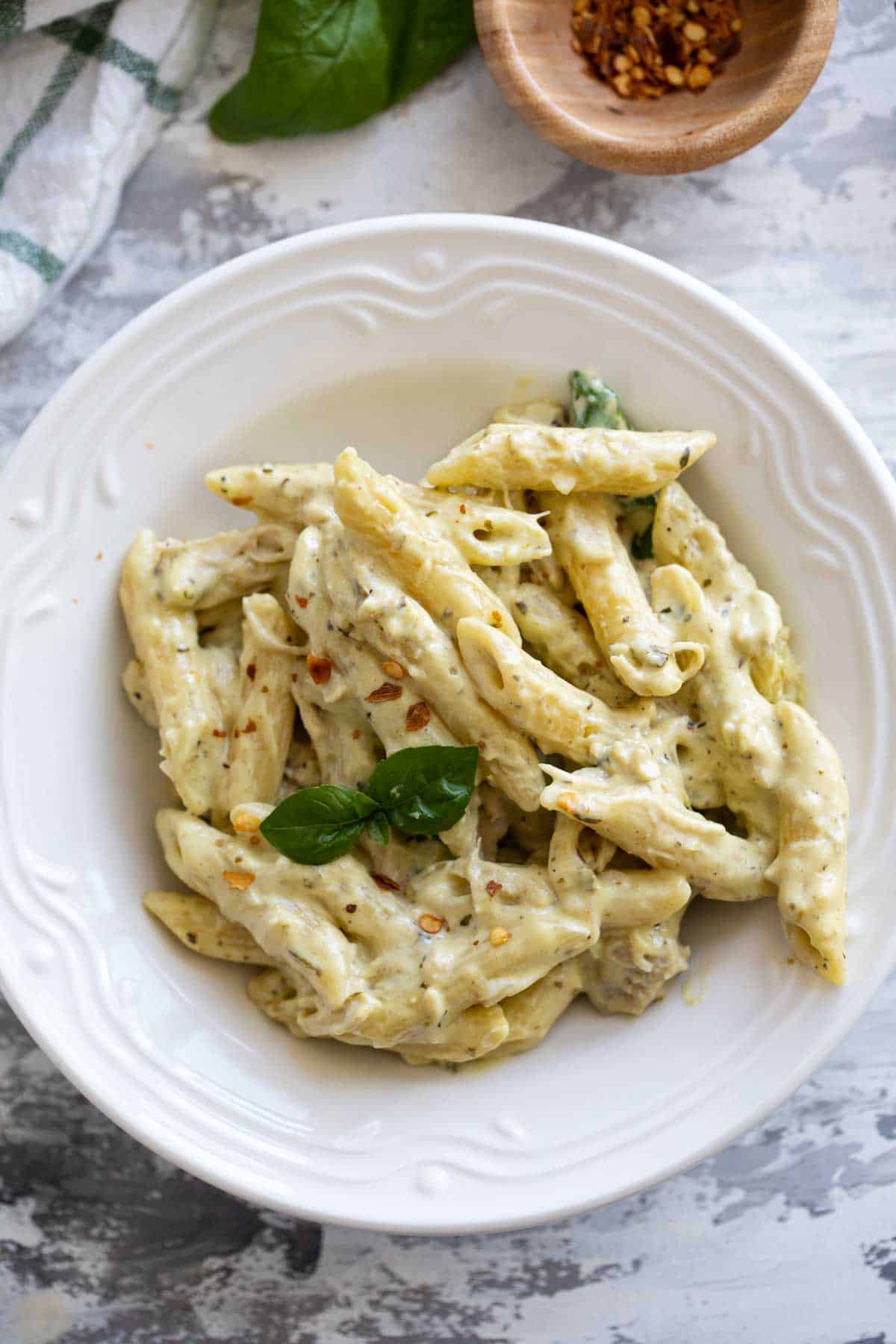 Bowl filled with chicken pesto pasta sprinkled with red pepper flakes.