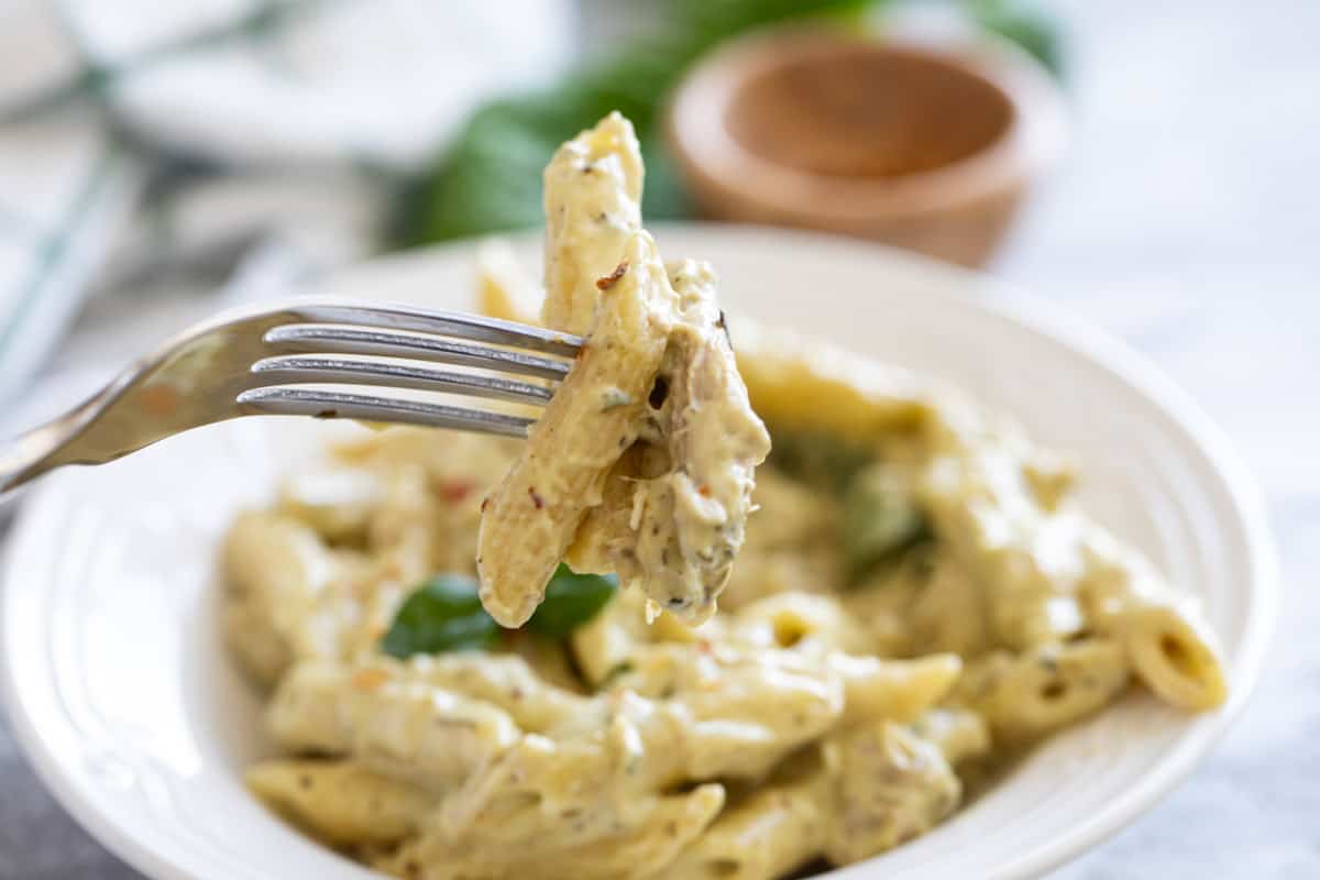 Fork with pasta and chicken with a bowl of the pasta behind.