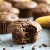 Chocolate Banana Muffin with a bite taken from it with mini chocolate chips around the muffin.